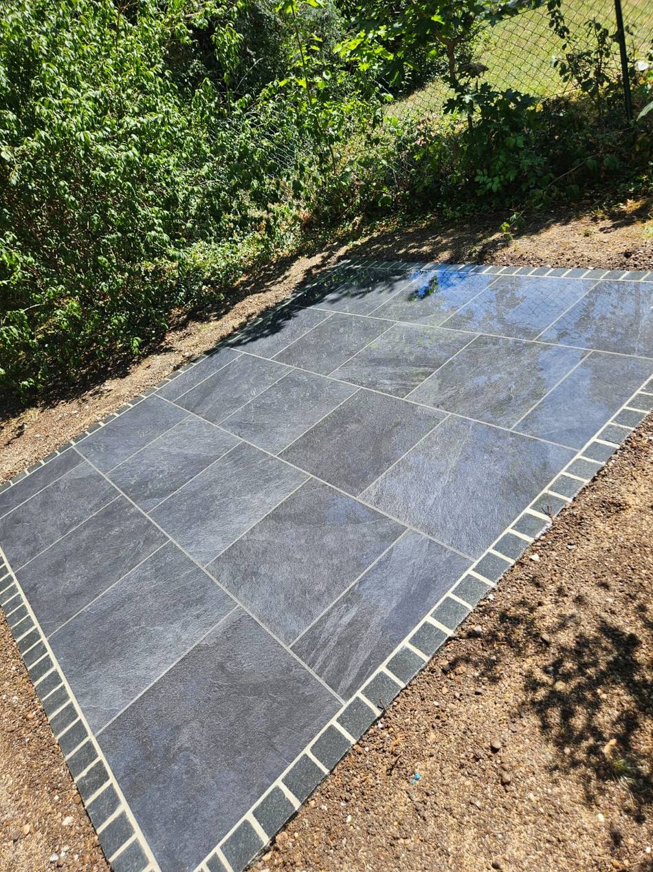 Neu verlegte Terrasse aus anthrazitfarbenen Feinsteinzeugplatten mit Pflasterrand