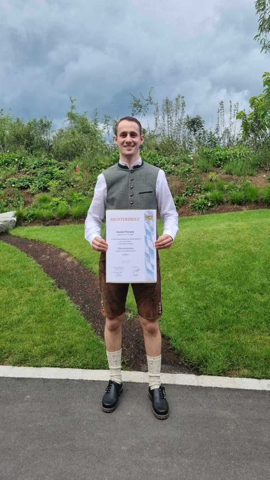 Daniel Premm in bayerischer Tracht mit seinem Meisterbrief im Garten- und Landschaftsbau
